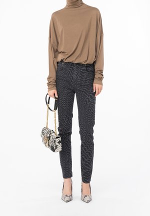 Kvinde iført en brun langærmet rullekrave, sorte bukser med mønster, bærer en sort og hvid taske med kædestrop, og hæle med slangeskinds-mønster.