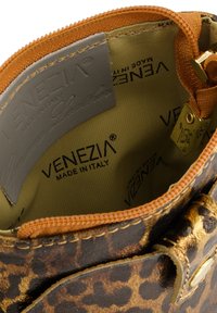 Indersiden af en leopardmønstret lædertaske med guldfarvet hardware, udstyret med en beige foring prydet med "VENEZIA" og en lynlåslukning.