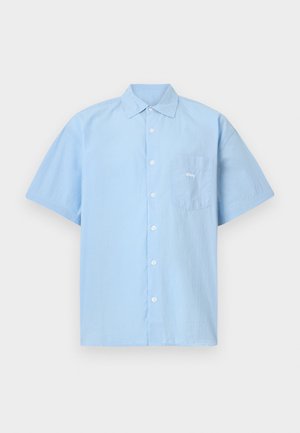 Chemise à manches courtes bleu clair en coton, boutonnée sur le devant. Elle comporte une poche poitrine avec le mot "obey" brodé en blanc.