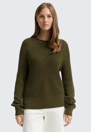 Maglione a maglia verde oliva con texture a coste, scollatura rotonda e maniche ampie. Completato con un orlo a coste, indossato sopra pantaloni bianchi.