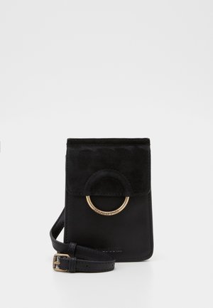 Sac bandoulière en cuir noir avec détail d'anneau circulaire doré et bandoulière réglable sur un fond blanc uni.