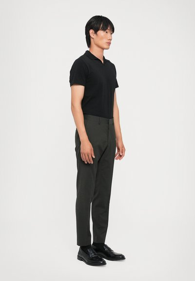 Sort polo-shirt, slim-fit mørkegrønne bukser og sorte loafers. Glat stof, korte ærmer og minimalistisk design uden mønstre.