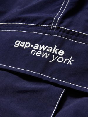 Navy fabric with white embroidered text "gap awake new york" and visible white stitching details on the garment.