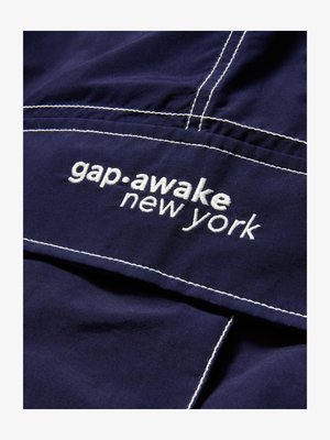 Tamsiai mėlynas audinys su baltu siuvinėtu tekstu "gap awake new york" ir matomomis baltomis siūlėmis ant drabužio.