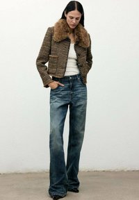 Chaqueta corta de tweed marrón con cuello de piel, combinada con jeans de tiro alto y pierna ancha en azul desgastado y zapatos negros de punta.