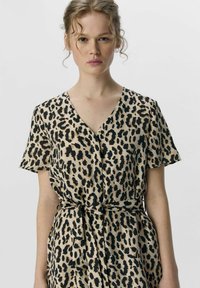 Robe à motif léopard en beige et noir, avec des manches courtes, un décolleté en V, et un détail de taille nouée pour une silhouette définie.