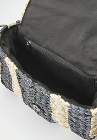 Borsa tessuta con esterno a righe nere e beige, dotata di un interno nero, tasca con zip e chiusura a scatto frontale.