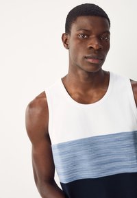 Canotta senza maniche con sezione superiore bianca, striscia orizzontale azzurro chiaro e fondo blu scuro. Realizzata in tessuto liscio e leggero.