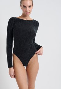 Czarny bodysuit z długim rękawem, wykonany z błyszczącej, fakturowanej tkaniny, z wysokim wycięciem nogawki i okrągłym dekoltem, charakteryzujący się dopasowanym krojem.