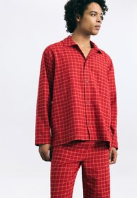 Red checkered pajama set made of soft fabric, featuring a collared button-up shirt and matching pants with a relaxed fit and long sleeves.