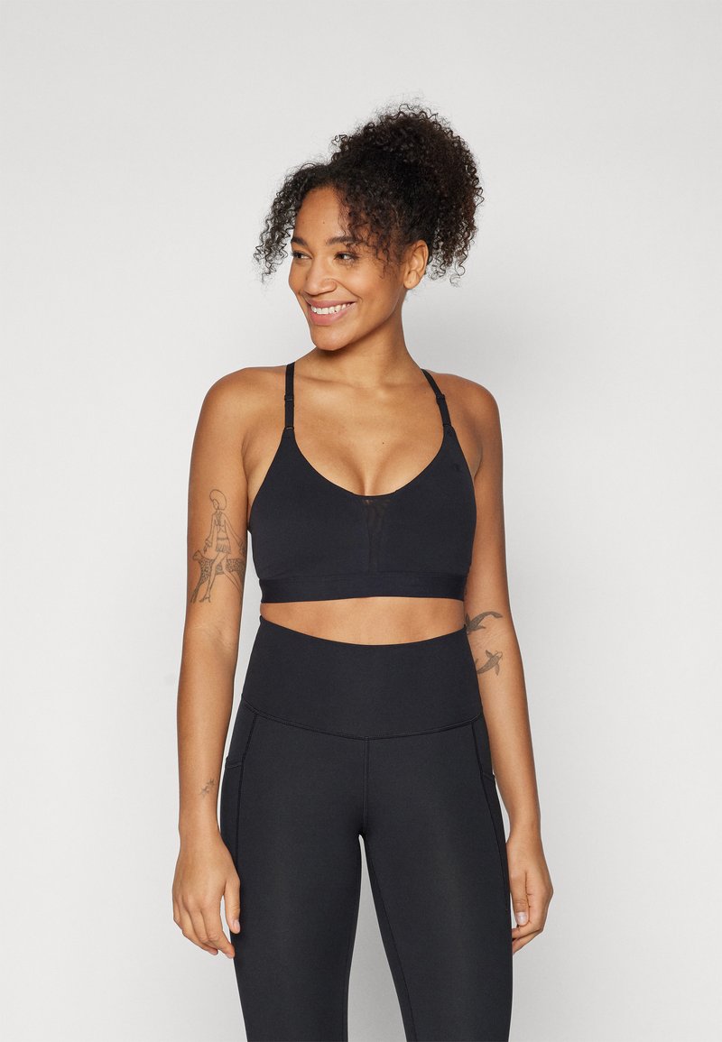 Sujetador deportivo negro con correas ajustables, un escote en V profundo y un diseño sin costuras. Combinado con leggings negros de tiro alto con bolsillos laterales.