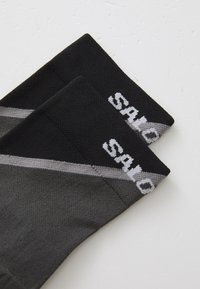 Calcetines negros y grises con un diseño de punto texturizado. Presentan texto de logo en blanco y un patrón de rayas diagonales en la parte superior.