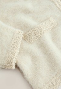 Hellbeige gestrickter Pullover mit einer weichen, flauschigen Textur, einer kleinen aufgesetzten Tasche und Rippdetails an den Bündchen und dem Saum.