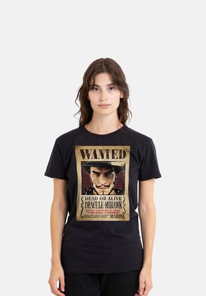 Junge Frau mit langen braunen Haaren trägt ein schwarzes T-Shirt mit einem Vintage-Gesuchtsplakat eines Mannes, der als "Dracule Mihawk." bezeichnet wird