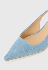 Vaaleansininen farkkukankainen slingback-korkokenkä, jossa on teräväkärkinen muotoilu, sileä sisävuori ja avoin kantapää. Omistaa teksturoidun kankaan pinnan.