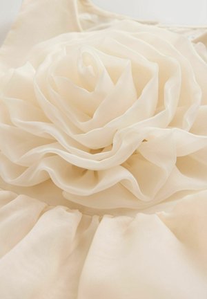 Crèmekleurige stoffen bloem gemaakt van gelaagd, doorschijnend materiaal, met zachte, vloeiende blaadjes die in een spiraalvorm zijn gerangschikt, met samengeplooide stof eronder.