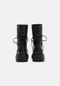 Black leather combat boots with a chunky sole, lace-up design, and elastic accents at the back. Smooth texture and stitched detailing.
