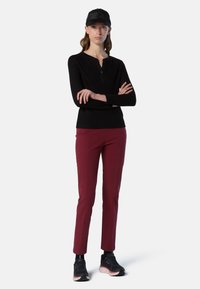 Camiseta negra de manga larga con cuello henley, combinada con pantalones burdeos ajustados y zapatillas negras con detalles en rosa. Se incluye una gorra negra.
