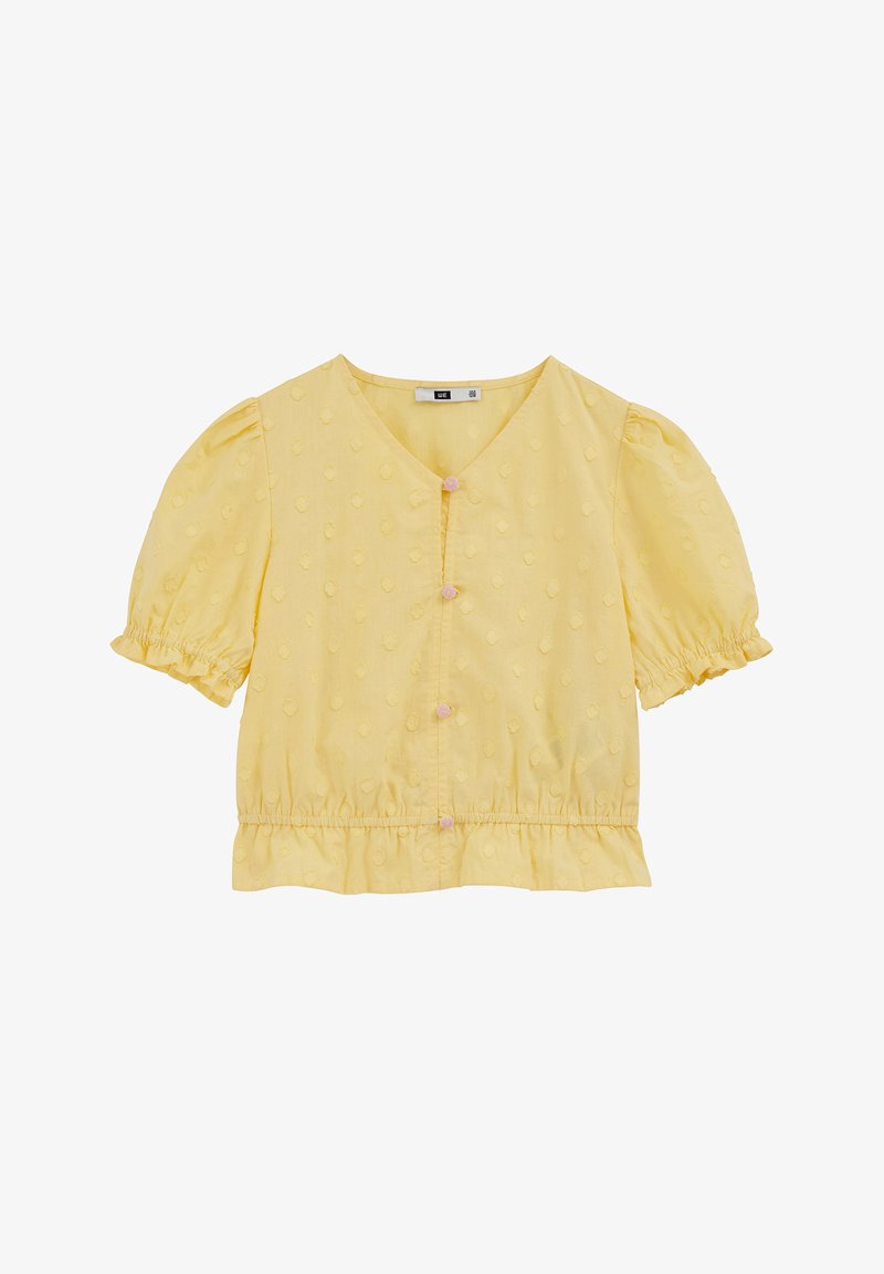 Blouse jaune à manches courtes avec un col en V, des pois texturés, des manches bouffantes froncées et un ourlet à volants, ornée de boutons roses sur le devant.
