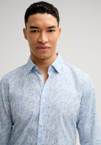 Camicia button-up di colore azzurro chiaro con motivo floreale, dotata di colletto, bottoni frontali e maniche lunghe. Realizzata in tessuto leggero.