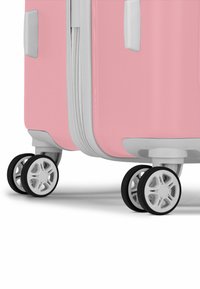 Pink hardshell luggage with textured surface, featuring gray accents and four spinner wheels with black tires and white rims for mobility.