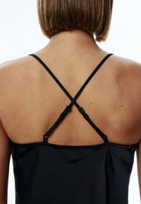 Zwarte satijnen camisole met dunne, verstelbare kruislings gedragen bandjes en een gladde textuur, die een clean, minimalistischer ontwerp toont.