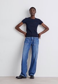 Tricou navy cu mânecă scurtă, asortat cu blugi denim albaștri, largi, care au buzunare frontale și cusături contrastante, purtat cu pantofi negri.