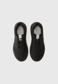 Black athletic shoes with a mesh upper, textured accents, round toe, and contrasting shoelaces featuring white and red details.