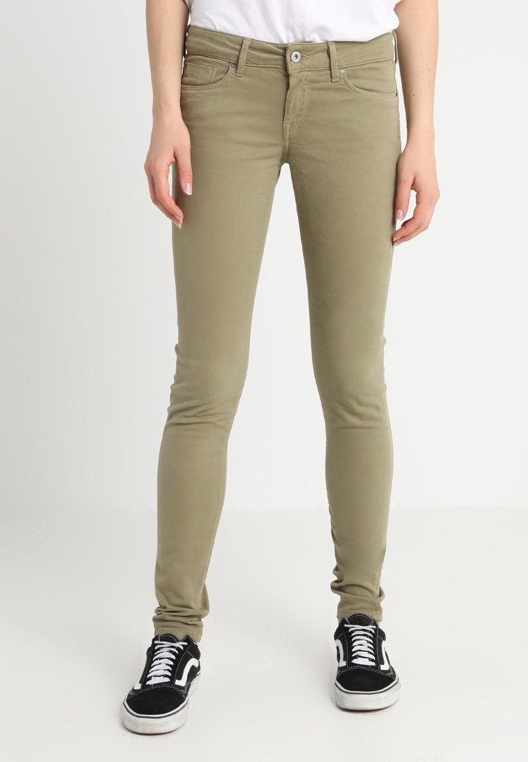 Jeans skinny verde oliva en tejido elástico, con cierre de cremallera, cinco bolsillos y herrajes en tono plateado, combinados con zapatillas negras.