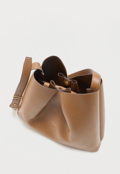 Καφέ δερμάτινη τσάντα ώμου με ρυθμιζόμενο λουρί, ανοικτό πάνω μέρος και πολλαπλά εσωτερικά διαμερίσματα σε λευκό φόντο.