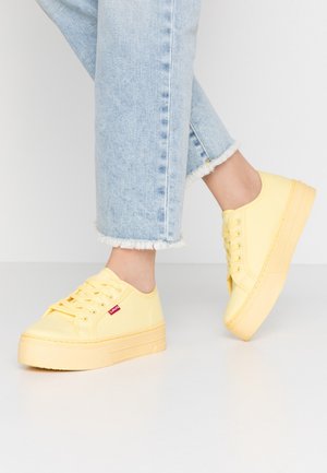 Stopy w jasnoniebieskich jeansach z postrzępionym dołem oraz pastelowożółtych sneakersach na platformie z sznurowadłami i małą czerwoną metką Levi’s.
