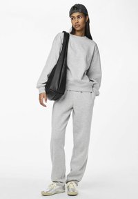 Sudadera gris y pantalones de chándal hechos de una tela suave, combinados con zapatillas plateadas y una bolsa negra holgada, presentando un ajuste y diseño casual.