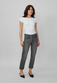Black high-waisted jeans with a straight cut, paired with a fitted white ribbed t-shirt. Flat black shoes complete the outfit.