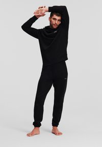 Schwarzes Sweatshirt mit hohem Kragen und engen Bündchen, kombiniert mit schwarzen Jogginghosen, die elastische Knöchel-Bündchen und ein kleines Logodetail aufweisen.