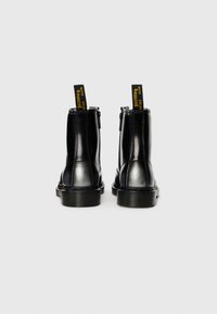 Mustad mustad ja läikiva viimistlusega mustad nahast pahklaiused saapad, tagumiste tõmblukkudega ja kontrastsete kollaste siltidega, millel on kirjas "WITH SOLES Bouncing." Paks kummist tald.