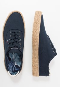 Zapatos de lona azul marino con suela de esparto texturizada, con cierre de cordones y un patrón floral en el interior. Diseño clásico de punta redonda.