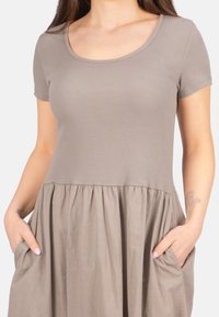 Beige kurzes Kleid mit kurzen Ärmeln, einem gerippten Oberteil und einem schwingenden, gerafften Rock. Mit seitlichen Taschen und einem weichen, strukturierten Stoff.