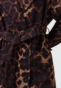Cappotto leopardato con una palette di colori marrone scuro e beige, dotato di una vita accentuata da una cintura, colletto a revers, grandi bottoni e tasche laterali.