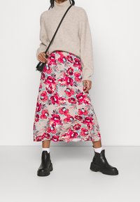 Knee-length floral skirt in beige with red and blue flowers, paired with a light brown knit sweater and black platform ankle boots.