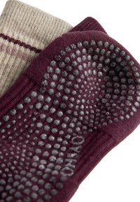 Dve páry ponožiek; jedny bordové s textúrovanými bodkami na chodidle, druhé béžové s pleteným pruhovaným vzorom pri manžete.