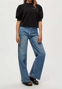Černý top s balónovými rukávy a kulatým výstřihem, spárovaný s širokými světle modrými džíny s roztrhanými lemy a černými plochými sandály.