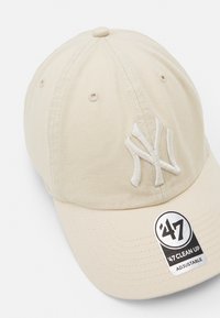 Beige Kappe mit gesticktem weißen "NY"-Logo, verstellbarem Riemen und runder Krone, aus strapazierfähigem Baumwollmaterial gefertigt.