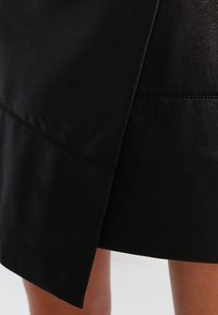 Svart läderkjol med en jämn yta, som har en sidoklyvning och skräddarsydda sömmar för en figurnära look.