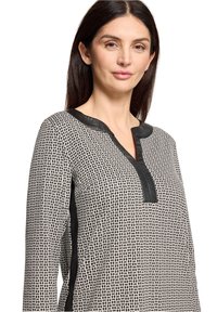 Zwart-wit top met een patroon en een V-hals, voorzien van een zwarte leren bies langs de halslijn en zijkanten, gemaakt van een zachte stof.