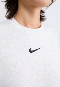 Grijze crewneck sweatshirt van een zachte stof met een klein zwart Nike-logo op de borst. Ribbelachtige hals en gestructureerd materiaal.