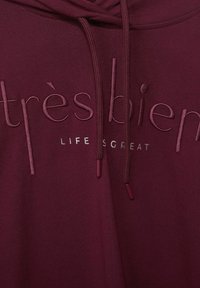 Bordowa bluza z nadrukiem "très bien" w haftowanej aplikacji oraz napisem "LIFE IS GREAT" w srebrnym kolorze. Zawiera sznurki z dopasowanymi zakończeniami.