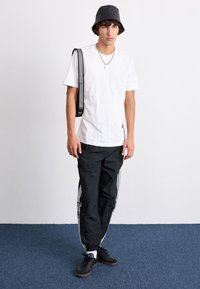 Balta T-krekls, melns ratu cepure, melni sporta bikses ar baltām svītrām un melnas kurpes. Sudraba ķēdes kakla aksesuārs. Vienkāršs dizains.