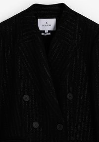 Sort dobbeltradet blazer med metalliske striber. Har notched klapkraver og to forreste knapper, lavet af tekstureret stof.