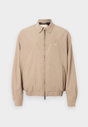 Veste bomber beige avec une fermeture éclair sur le devant, un col pointu, une taille élastique et un logo "EA" brodé sur le côté gauche supérieur.