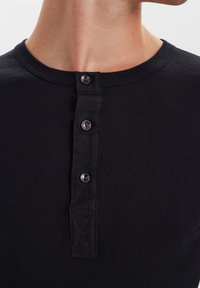 Black ribbed henley shirt with three buttons and a crew neckline. Features a textured fabric and a reinforced placket for durability.